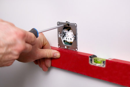 An electrician uses a screwdriver to install an electrical outlet on a white wall. A worker uses a building level to check that the level is correct.の写真素材