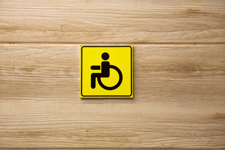 Yellow sign featuring a black wheelchair symbol displayed on a wooden wall to indicate accessible facilities for individuals with disabilities. High quality photoの写真素材