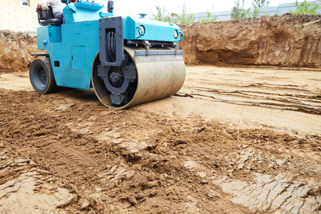 The compact roller actively compacts the soil at a construction site where excavation work has recently been carried out. Dust and soil are leveled when the sky is clear. Building a house.の写真素材