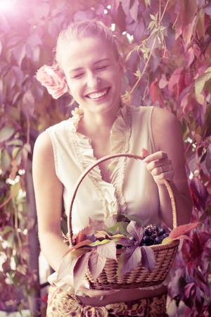 Beautiful girl in a long skirt with a basket of grapes outdoors shootingの写真素材