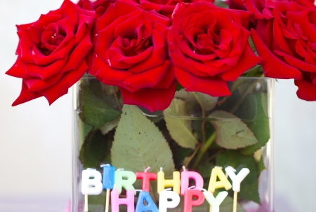 Candles of the letters "Happy birthday" in the background of a bouquet of red rosesの写真素材