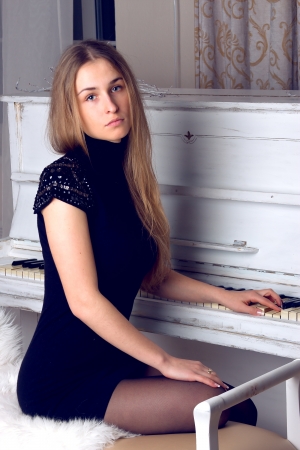 girl with blond long  hair in  dress playing white pianoの写真素材