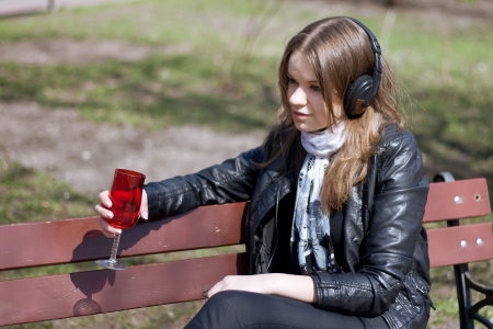 girl on a park bench drinking a glass of red wineの写真素材