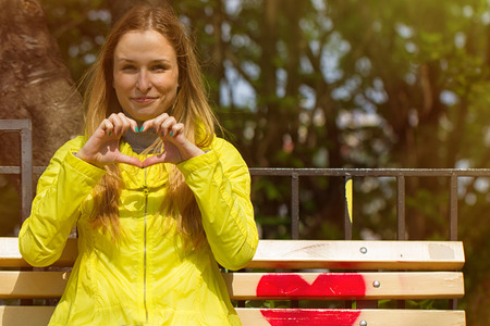 Girl folded her fingers in the form of heart. On a bench in the parkの写真素材
