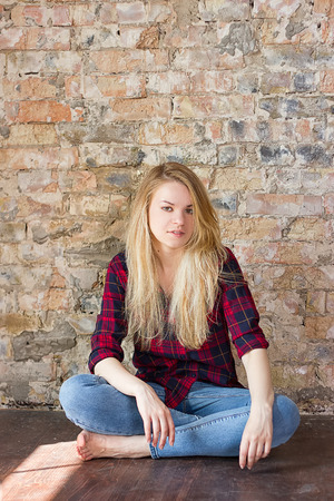 Front view of attractive white girl sitting on wooden floor against concrete wallの写真素材