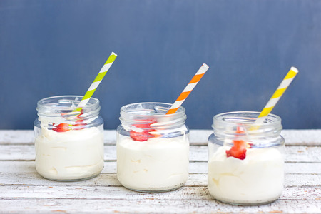 Three in a jar of yogurt with strawberries on a wooden board on a blue background