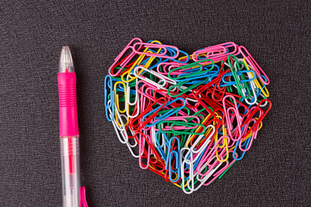 Variety of color paper clips arranged in heart shape on black background.の写真素材