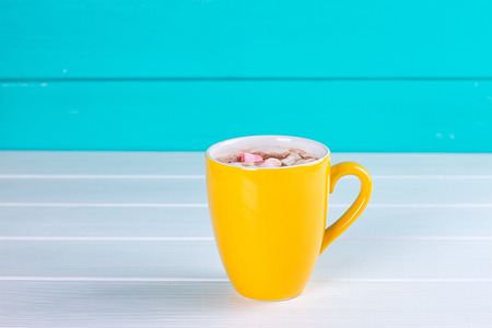 Yellow cup of hot cocoa with marshmallows on blue wooden backgroundの写真素材