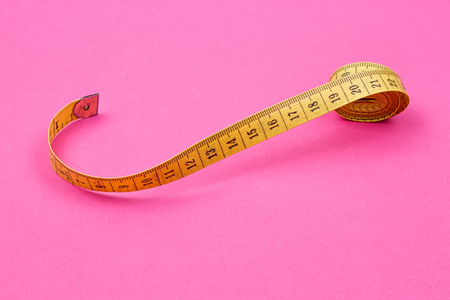 Measuring tape of the tailor on the pink background