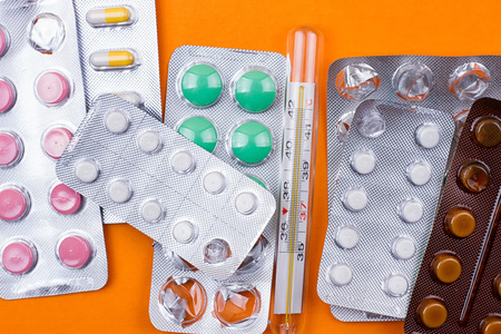 Different pills and thermometer on orange background