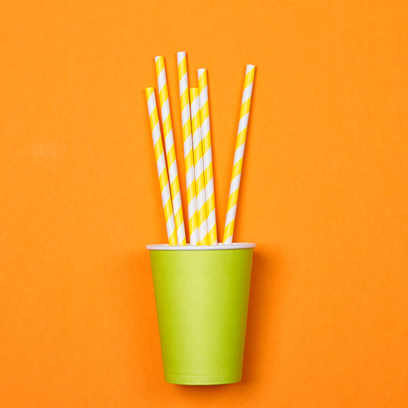 a bundle of multi-colored drinking straws in a paper Cup on a orange background. fashion minimal. flat layの写真素材