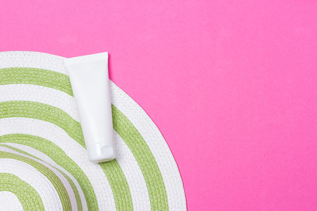 Beach green straw female hat and sun protection cream on a pink background