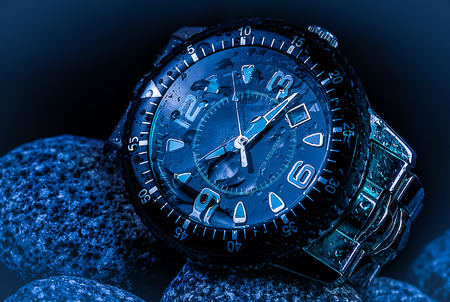 Closeup of wet metal wrist watch on blue rocks