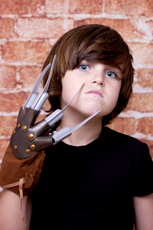 Kid with scary nails on face. Brick wall backgroundの写真素材