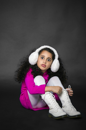 pretty little girl sitting on the floor in white bootsの写真素材