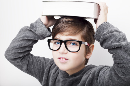Portrait of a little handsome boy kid in eyeglasses with book on a head. Isolated white background