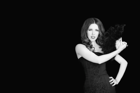 Beautiful woman in black dress holding fan of  feathers on dark studio backgroundの写真素材