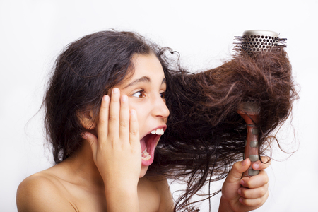 Hair care concept with portrait of girl brushing her unruly, tangled long hair isolated on whiteの写真素材