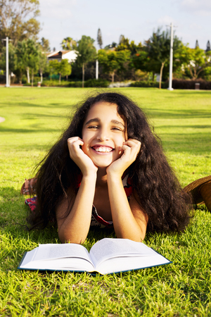 The little African girl laying on a grass in park with book and hatの写真素材