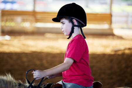 Portrait of little boy riding a horse. First lessons of horseback ridingの写真素材