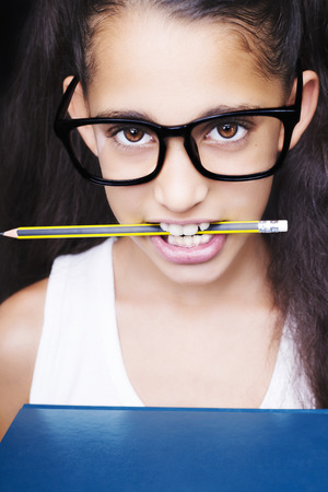 Image of a beautiful African young girl wearing glasses, holding book in her hands and pencil in her mouthの写真素材