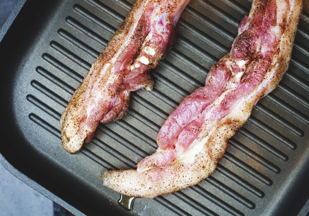Two pieces of pork meat sprinkled with pepper, fry in a frying pan on one side.