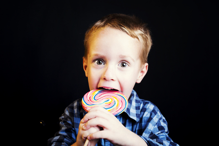 Young boy holding lollipop on black background.の写真素材