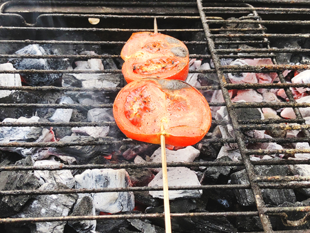 Fresh ripe red sliced tomatoes on a wooden stick grillingの写真素材