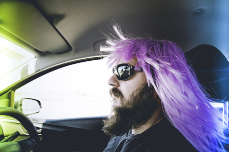 Bearded man in a pink wig behind the wheelの写真素材