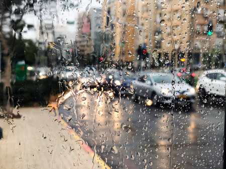 Rainy car and street lights seen through a windshield on a busy road at night.