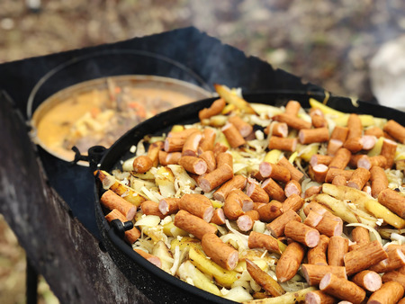 Hunting sausages with potatoes and onions in pan on fire.