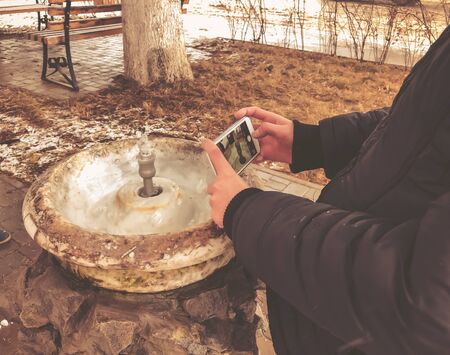 Child takes a photo. City fountain for drinking water flowing from the old marble column in city...