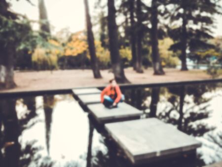 Attractive elegant girl in a red blouse posing in a park by the pond. Autumn day in the park. Blure effect.の写真素材