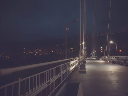 Sidewalk area going through a cable-stayed bridge with big steel cables, closeup at night time in...