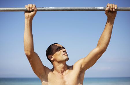 A male athlete with a naked torso is training on a horizontal bar.