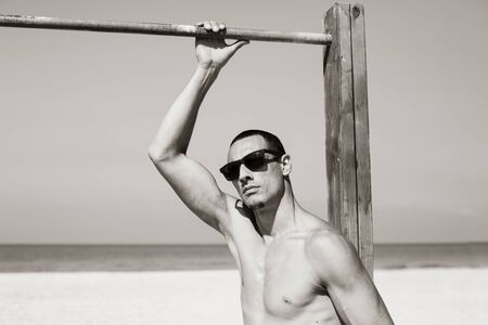 young muscular man resting and posing on the beach. Wearing sunglasses.