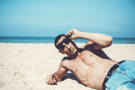 young muscular man resting and posing on the beach.の写真素材