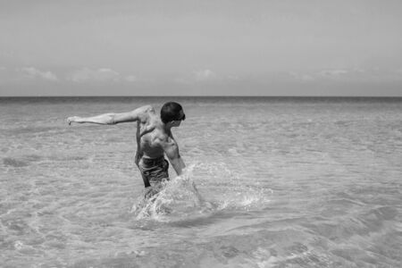 young muscular man posing and splashing around in the sea.の写真素材
