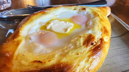 Hand mixing ingredients of adjarian khachapuri with fork in restaurant. Open bread pie with cheese and egg yolk. Yummy georgian cuisine.の写真素材