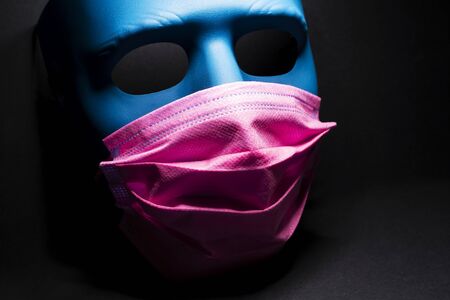 Medical pink mask put on a blue mask. black background.の写真素材