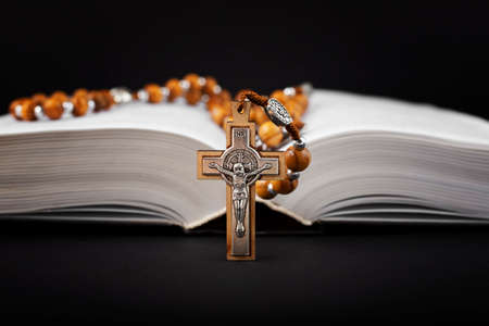 Traditional christian holy religious wooden rosary with bible on black background.