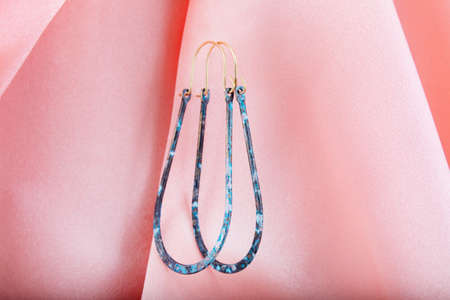 Blue metal earrings hanging on pink silk.の写真素材