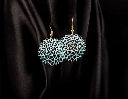 Round blue metal earrings hanging on black silk background.の写真素材