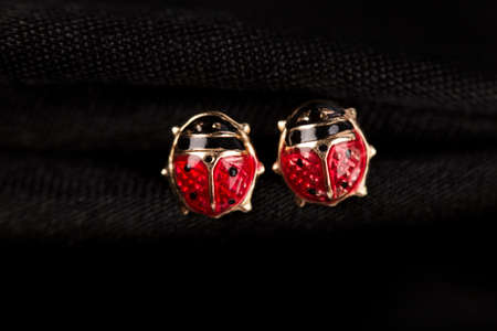 Ladybug-shaped gold stud earrings on black fabric background