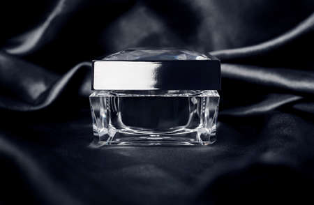 Cosmetic glass jar with a lid on dark silk fabric backgroundの写真素材