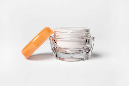 Cosmetic glass jar with a lid and cream on white background
