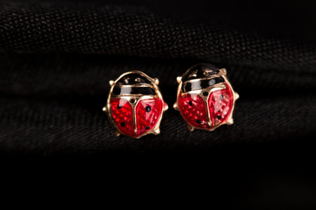 Ladybug-shaped gold stud earrings on black fabric backgroundの写真素材