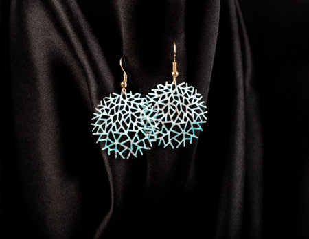 Round blue metal earrings hanging on black silk background.の写真素材