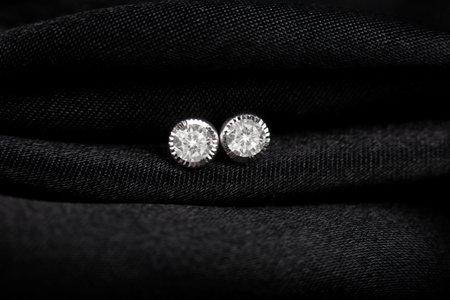Round silver stud earrings with diamond on black fabric background.の写真素材