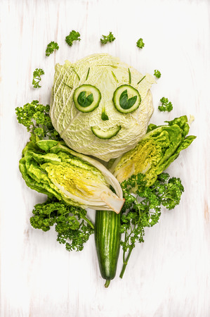 funny girl face made of  green vegetables, cucumber and lettuce on white wooden backgroundの写真素材